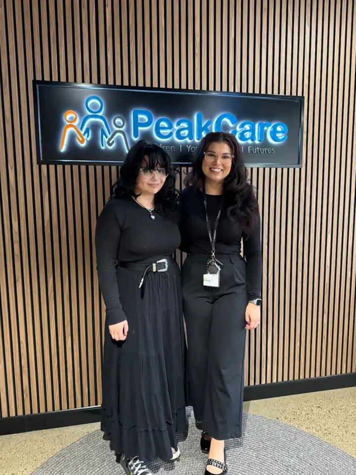 Carer and sibling standing in front of PeakCare sign