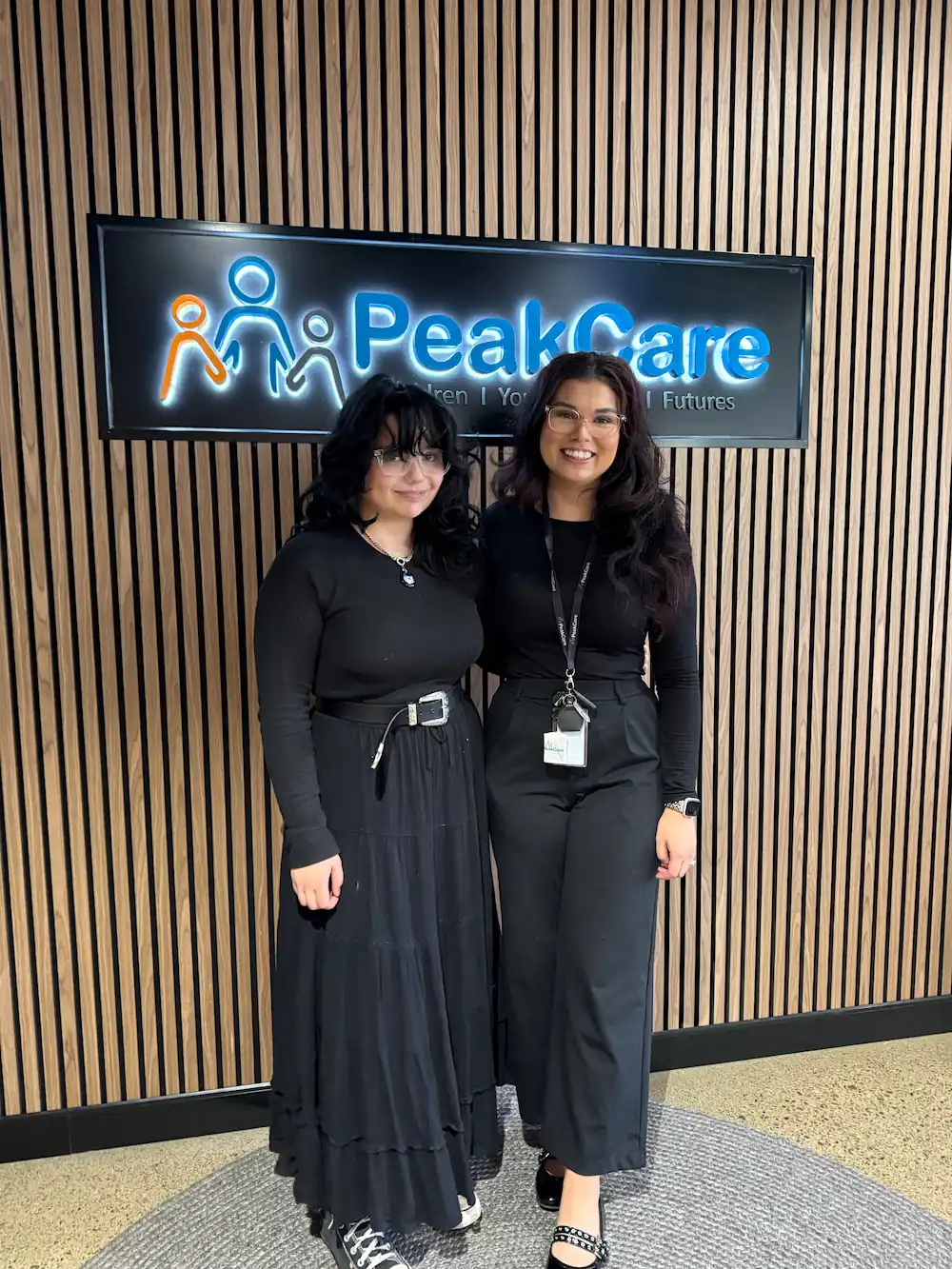 Carer and sibling standing in front of PeakCare sign